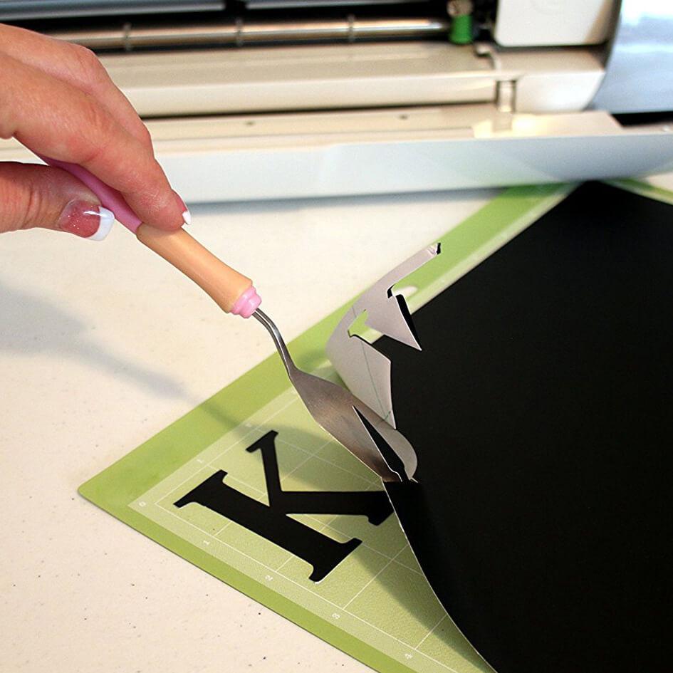 Black Matte vinyl sheet with hand holding a weeding tool after cutting out the letter K